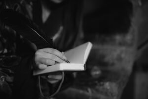 A hand writing in a notebook with a quill pen, captured in black and white for a classic feel.